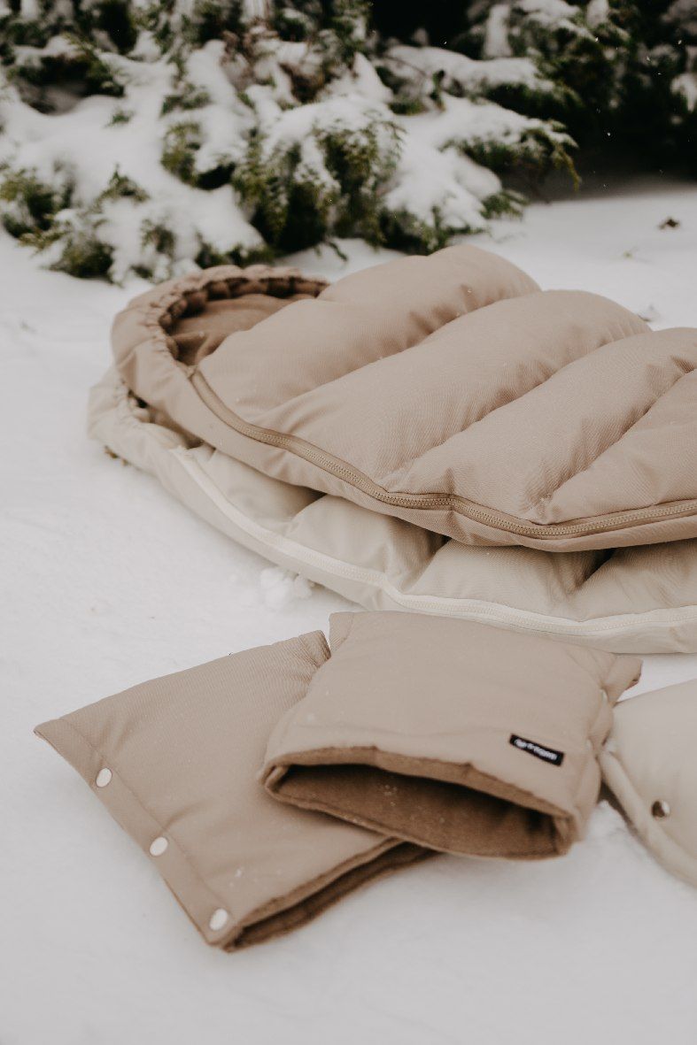 Gepolsterter, beiger Babyschlafsack mit Reißverschluss und passenden Fäustlingen im Schnee.