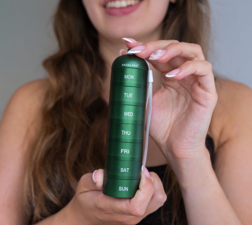 Frau hält eine grüne Pillendose mit 7 Fächern für die Wochentage.