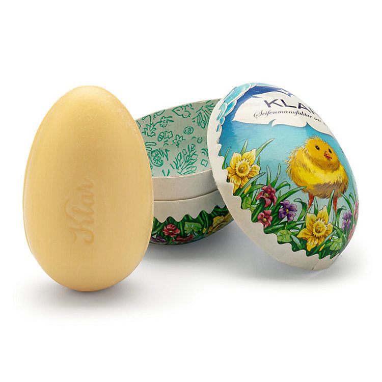 Eiförmige Seife neben geöffneter Osterei-Verpackung. Seife mit Schriftzug Klar. Verpackung mit Küken-Motiv und floralen Elementen.
