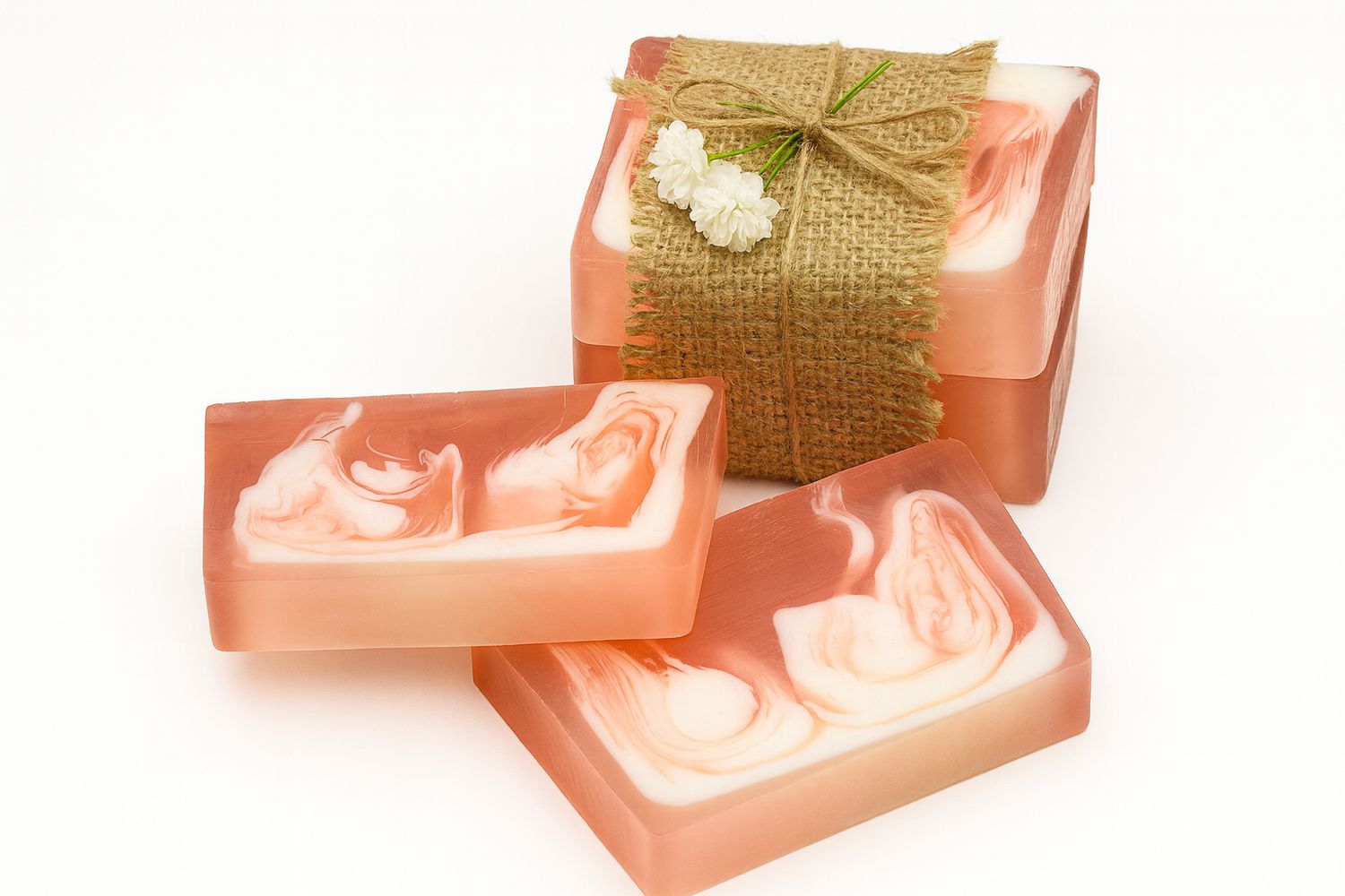 Mehrere rosa Seifenstücke mit weißer Maserung. Einige sind mit einem Juteband und Blumen verpackt.