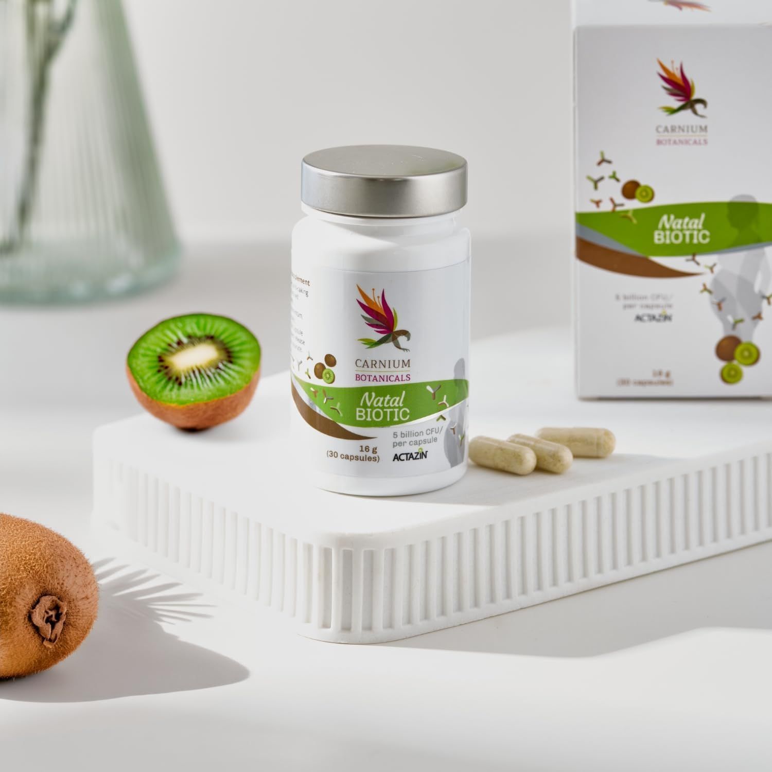 Weiße Flasche mit silbernem Deckel. Aufschrift: Carnium Botanicals Natal Biotic. Kiwi und Kapseln.