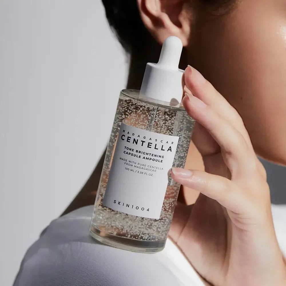 Klare Glasflasche mit Pipette. Aufschrift: CENTELLA, TONE BRIGHTENING CAPSULE AMPOULE. SKIN1004-Logo.