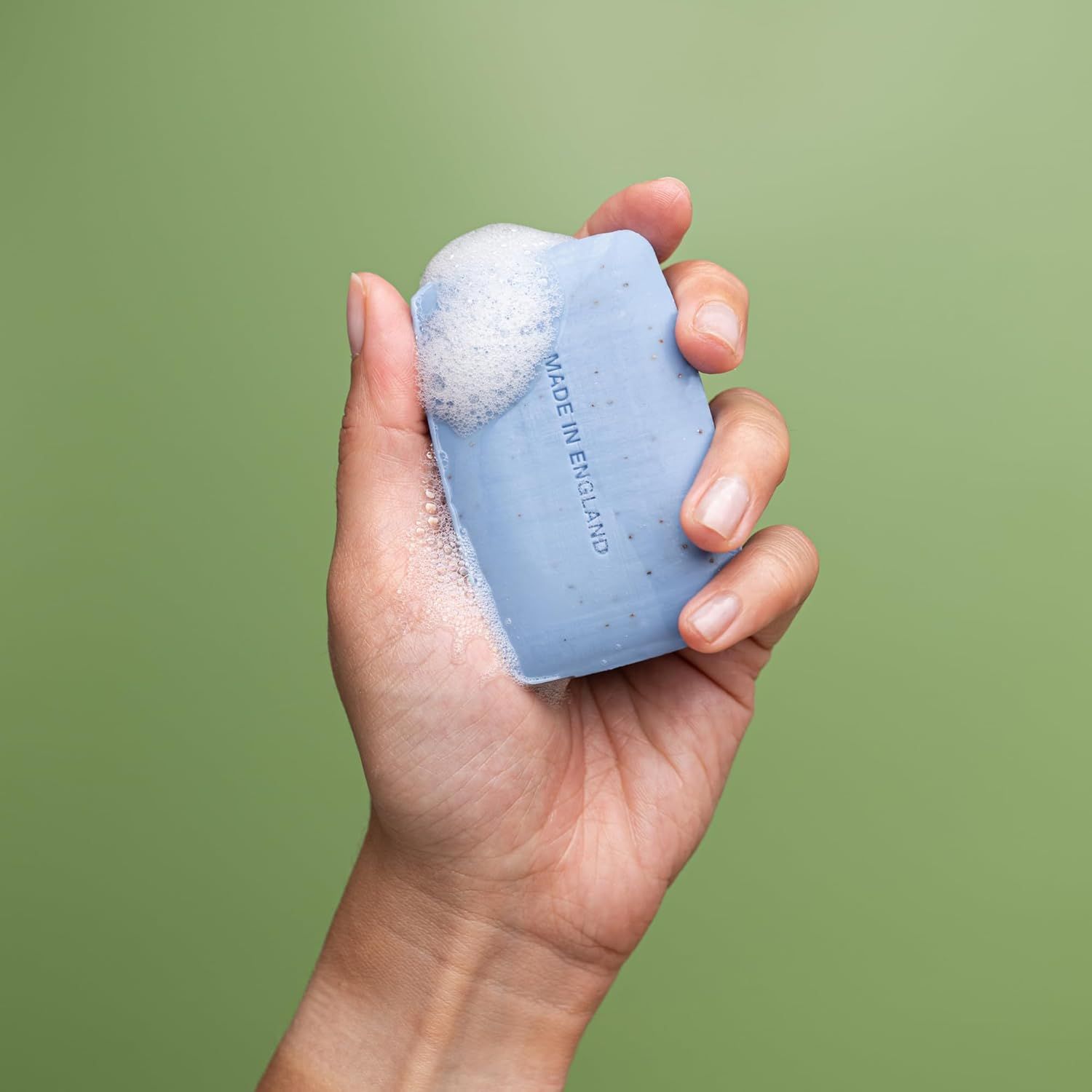 Hand hält blaues Seifenstück mit Schaum. Aufschrift: „MADE IN ENGLAND“.