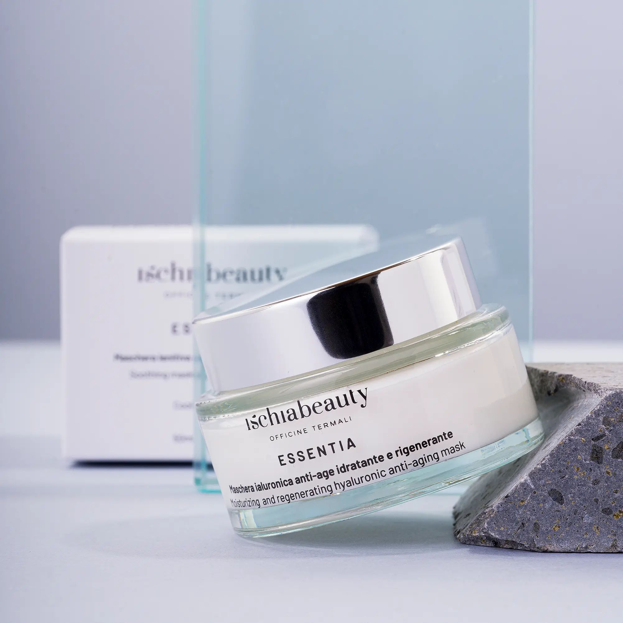 Glasbehälter mit Creme, silberner Deckel. Aufschrift: ischiabeauty ESSENTIA. Auf Stein.