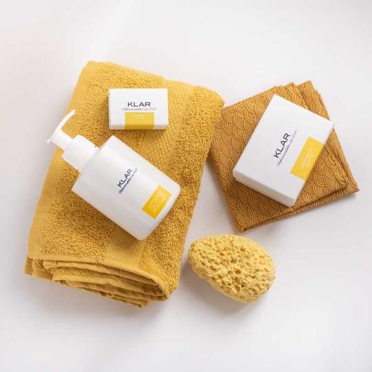 Zeep, zeepdispenser, spons en handdoek. Klar-logo op zeep en dispenser. Gele en oranje textiel.