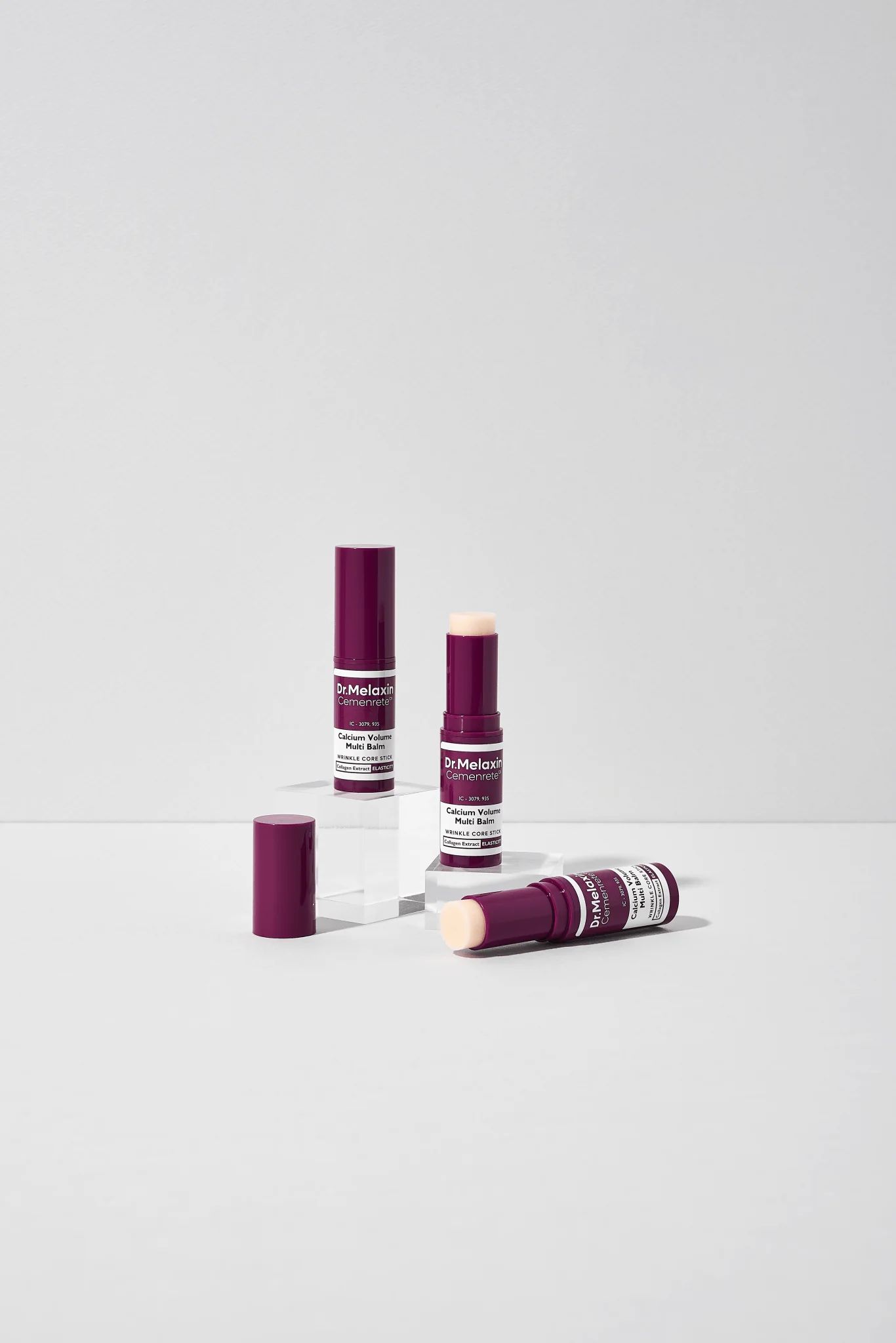 Drei dunkellila Balms. Aufschrift: Dr.Melaxin Cemenrete Calcium Volume Multi Balm. Weißer Text. Ein Balm liegt.