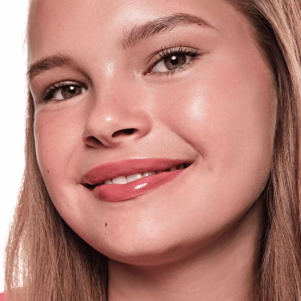 Porträt einer jungen Frau mit rosafarbenem Lipgloss. Sie lächelt. Der Lipgloss ist glänzend und betont die Lippen.