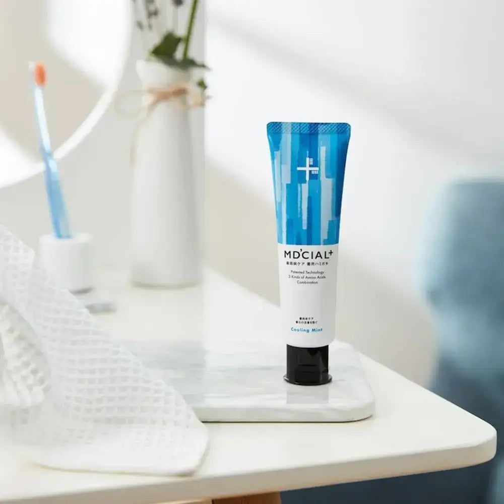 Zahncreme-Tube mit blauem, abstraktem Muster. Daneben eine Zahnbürste und ein Handtuch.