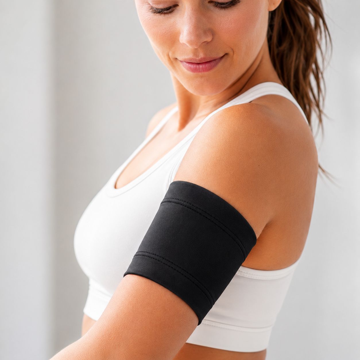 Schwarzer Armloop am Oberarm einer Frau. Lycra-Material. Nahtdetails. Trägt Sport-BH.