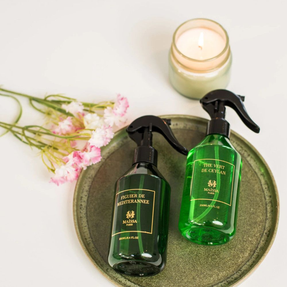 Zwei grüne Sprühflaschen mit schwarzem Sprühkopf auf einem Tablett. Kerze und Blumen.