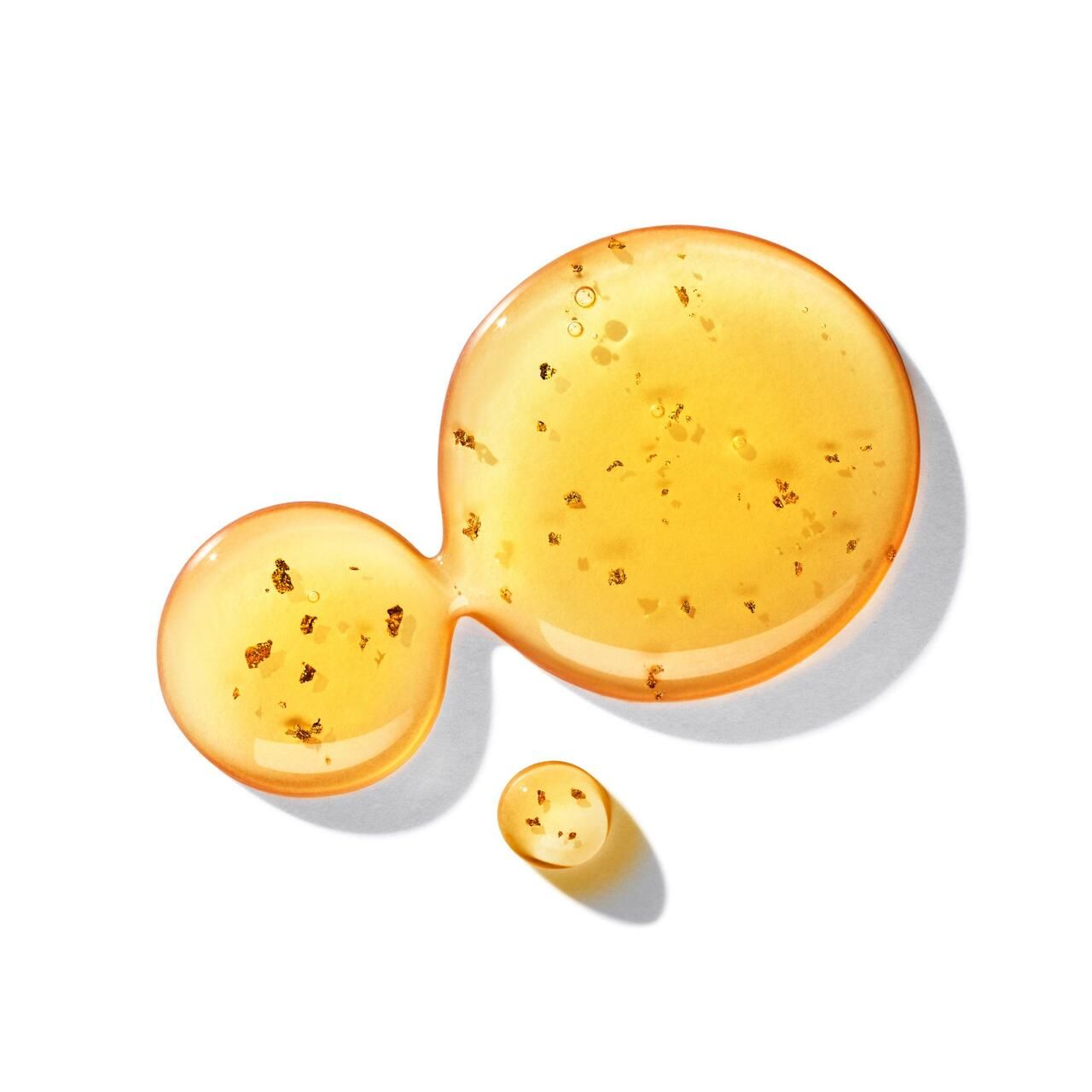 Goldfarbene Flüssigkeitstropfen mit goldenen Partikeln. Gezeigt auf weißem Hintergrund. 
