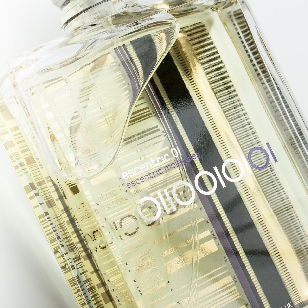 Nahaufnahme eines Parfümflakons. Rechteckige Form, transparente Flüssigkeit. Schwarze, violette und goldfarbene Streifen. Markenschriftzug.