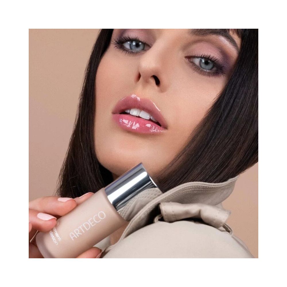 Frau hält Artdeco Rich Treatment Foundation. Flasche mit silbernem Deckel. Produktname und Marke sichtbar.