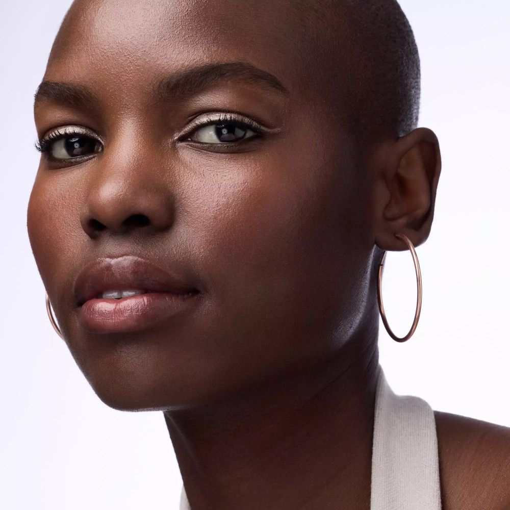 Porträt einer Frau mit dunkler Haut. Sie trägt goldfarbenen Eyeliner. Große goldfarbene Creolen.