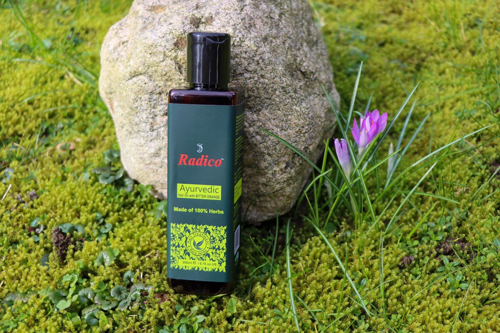 Braune Flasche mit schwarzem Deckel. Grün-gelbes Etikett mit "Radico" und "Ayurvedic". Auf Moos und Stein platziert.