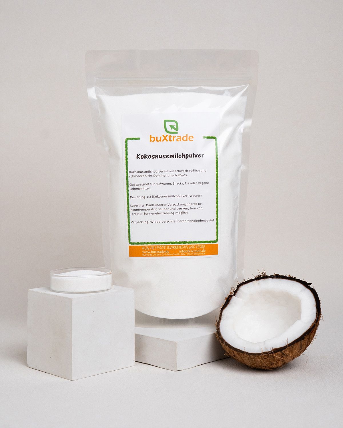 Verpackung von buXtrade Kokosnussmilchpulver, daneben eine halbe Kokosnuss und eine Schale mit Pulver.