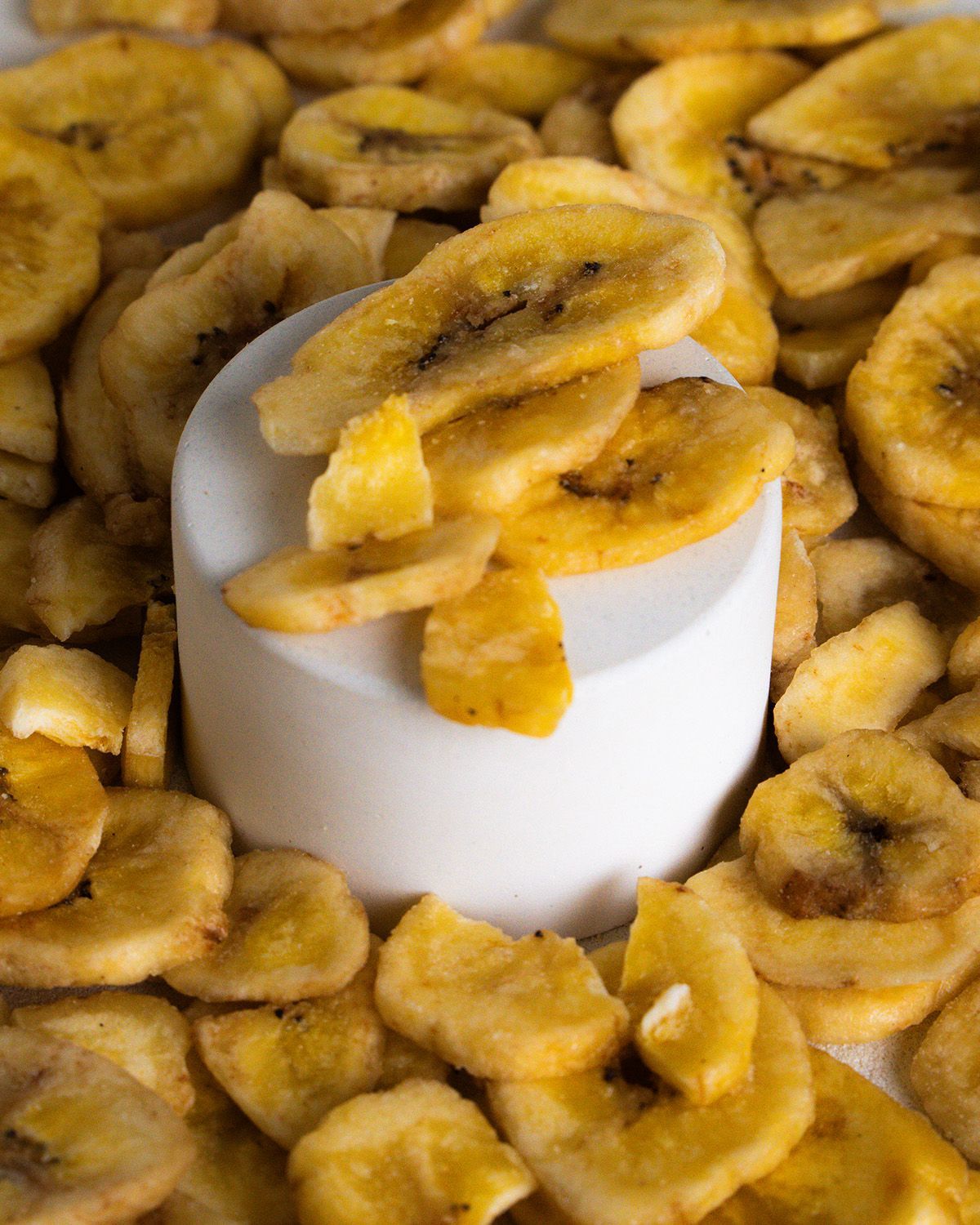 Nahaufnahme von Bio Bananenchips auf einem weißen Podest. Chips umgeben das Podest.