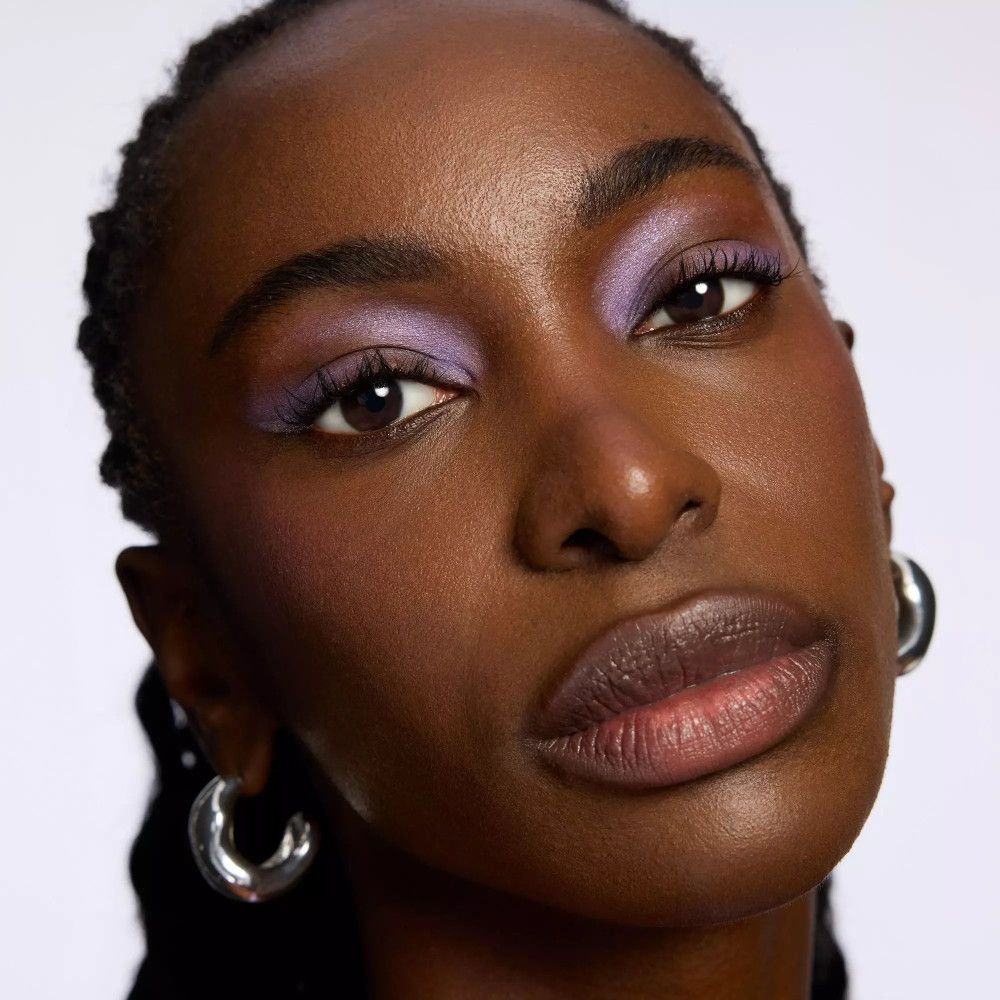 Porträt einer Frau mit dunkler Haut und lila Lidschatten. Große silberne Creolen.