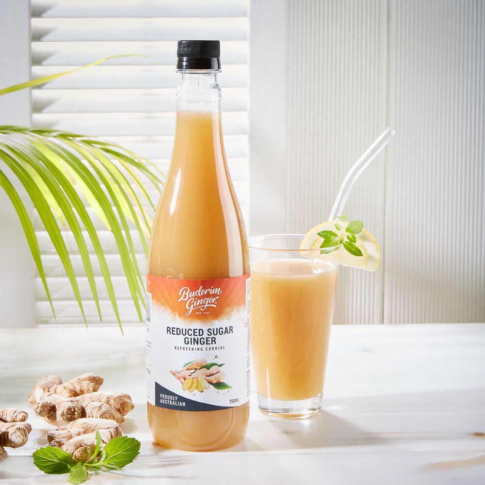 Ingwer-Refresher-Flasche neben Glas mit Getränk. Zitrone und Minze als Garnitur. Ingwerstücke und Blätter.