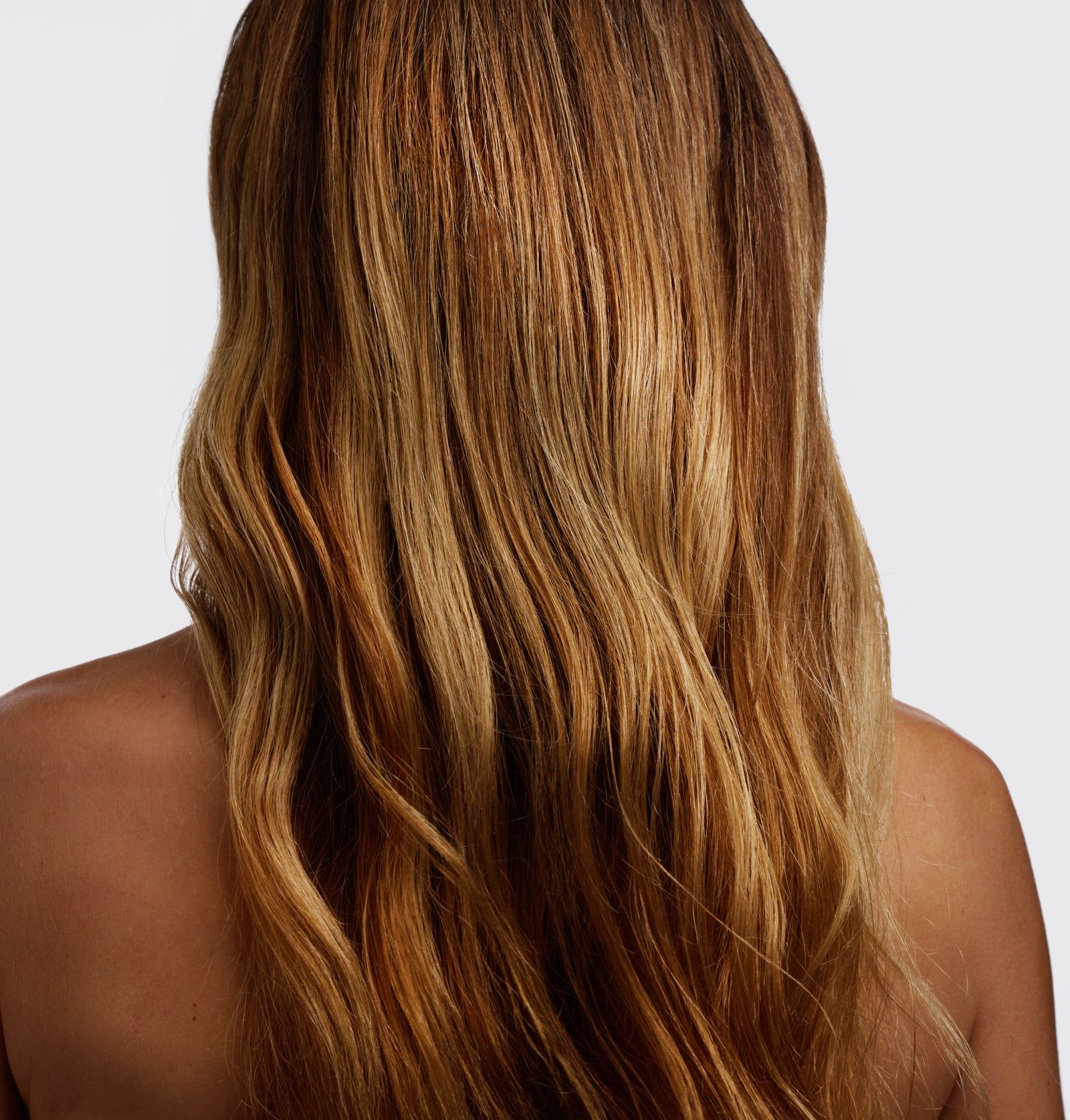 Rückansicht einer Person mit welligem, braun-blondem Haar. Das Haar ist schulterlang und hat verschiedene Farbtöne.