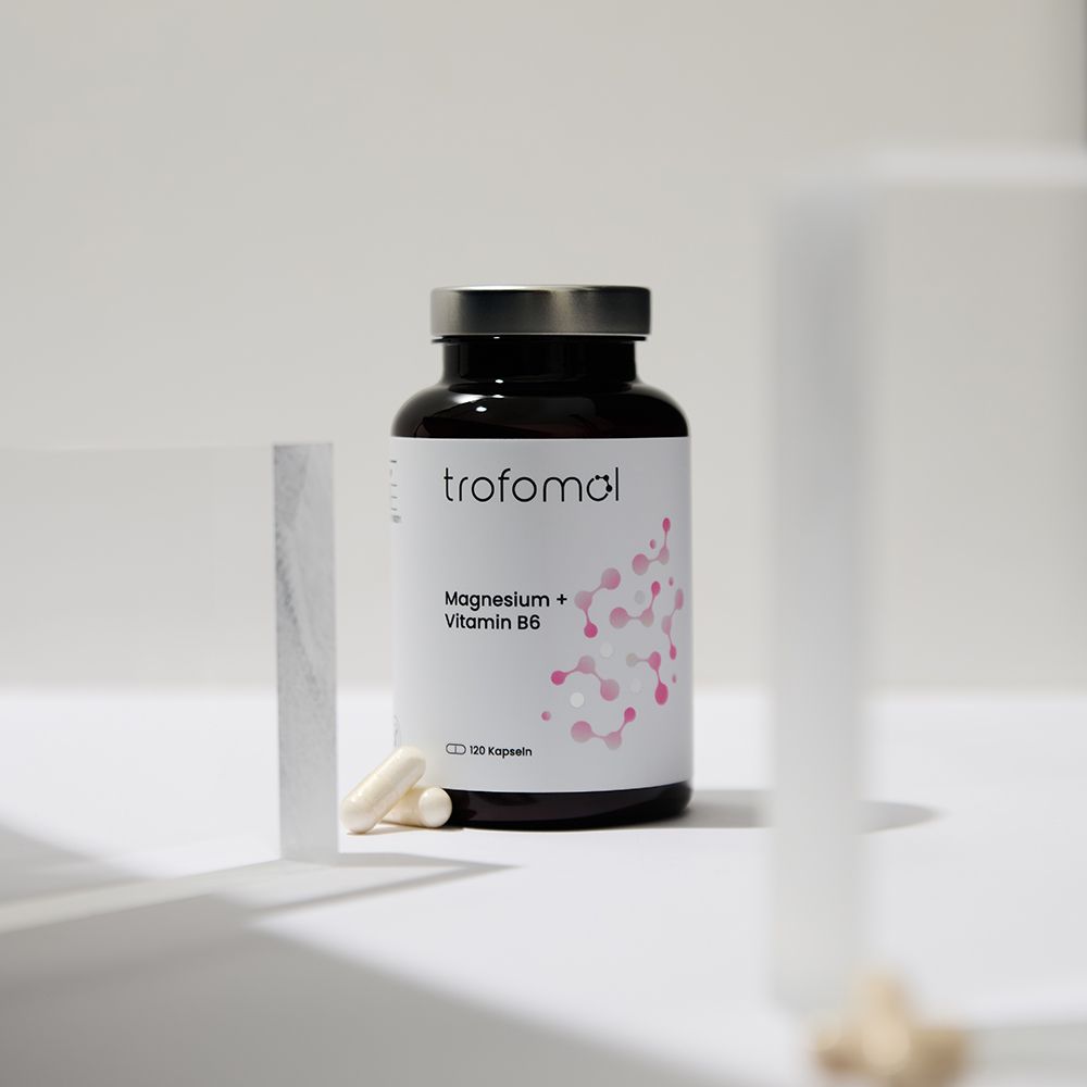 Braune Glasflasche mit weißem Etikett. Aufschrift: trofomol, Magnesium + Vitamin B6. Zwei Kapseln daneben.