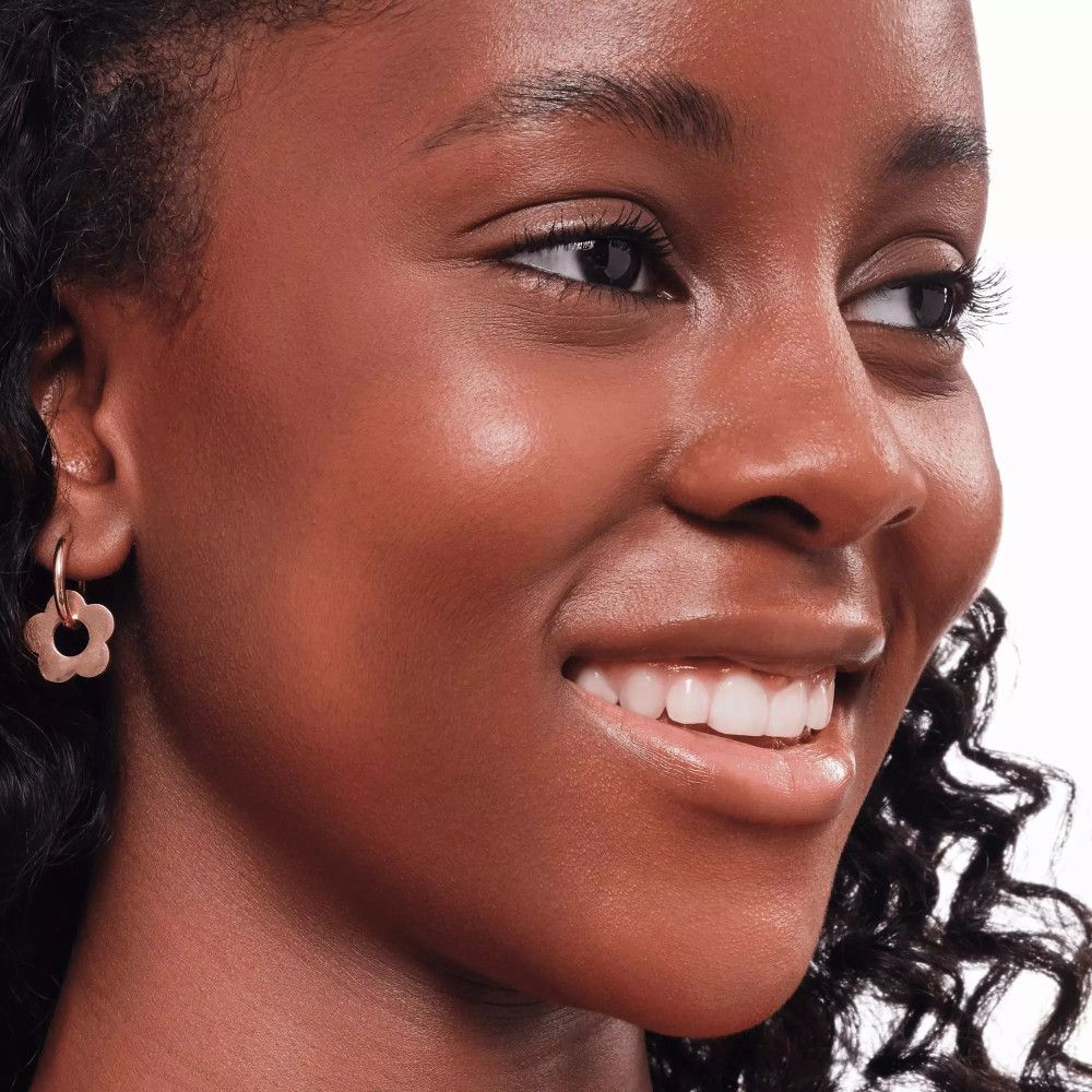 Porträt einer lächelnden Frau mit gebräunter Haut. Sie trägt goldene Ohrringe.