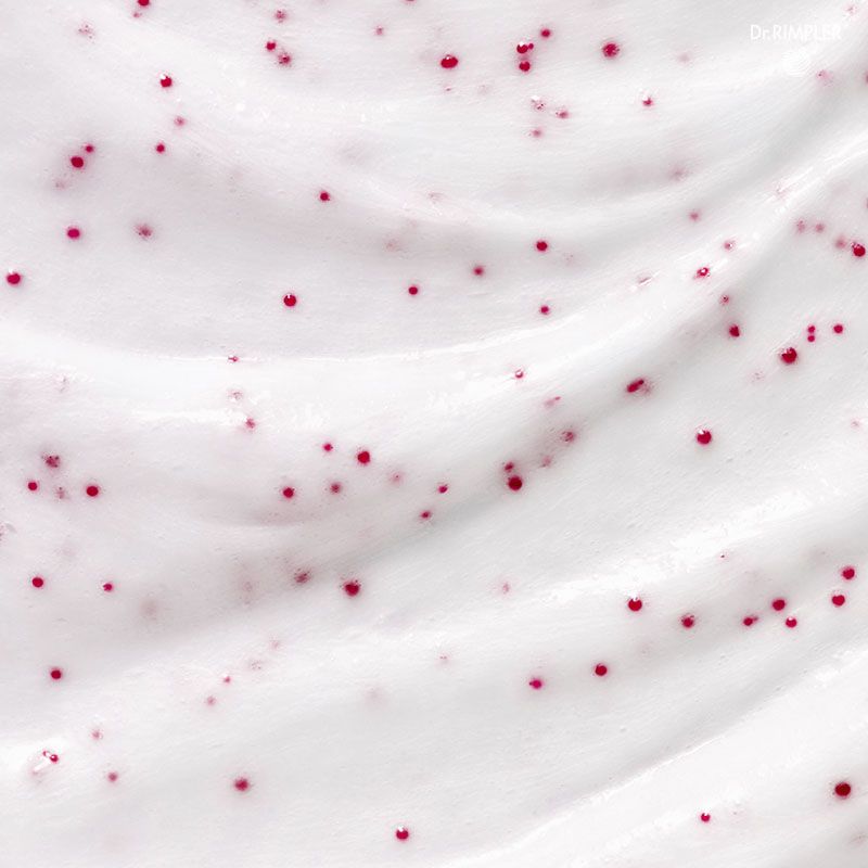 Nahaufnahme einer weißen Creme mit roten Partikeln. Die Creme ist gewellt.