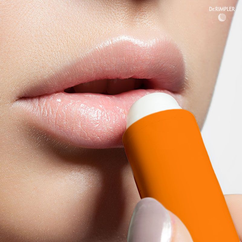 Person trägt einen orangefarbenen Sun Stick auf die Lippen auf. Der Stick hat einen weißen Stift. Aufschrift: Dr. RIMPLER.