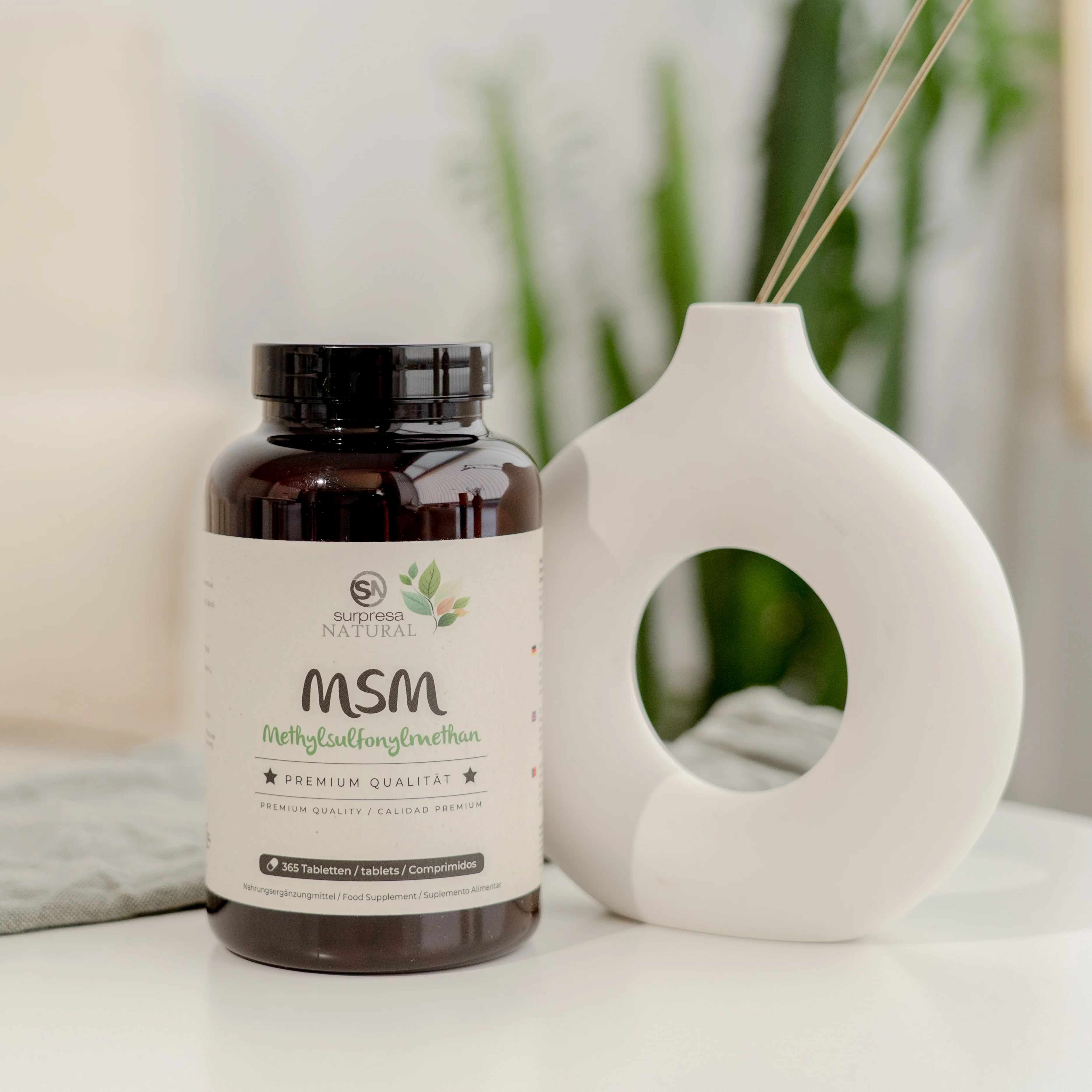 Braune Tablettenflasche mit Etikett. Aufschrift: Surpresa Natural MSM, Methylsulfonylmethan, Premium Qualität. 365 Tabletten. Neben Vase.