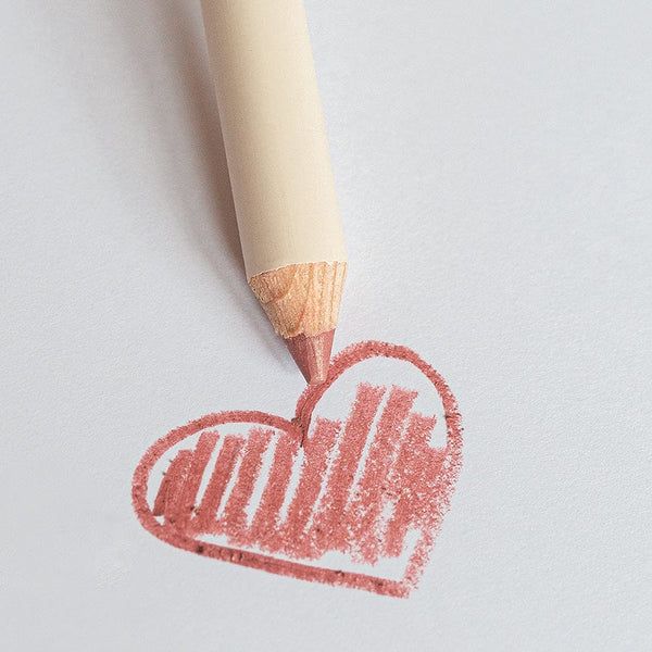 Lippenstiftstift zeichnet ein Herz auf weißem Papier. Stift und Herz sind rosafarben.