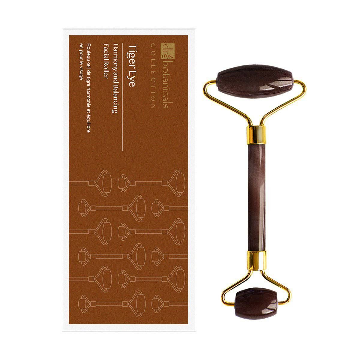 Gesichtsroller neben Verpackung. Roller mit goldfarbenem Griff und braunen Rollen. Verpackung mit Text.