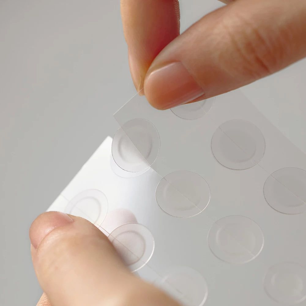 Hände entfernen einen transparenten, runden Patch von einer Blisterpackung.