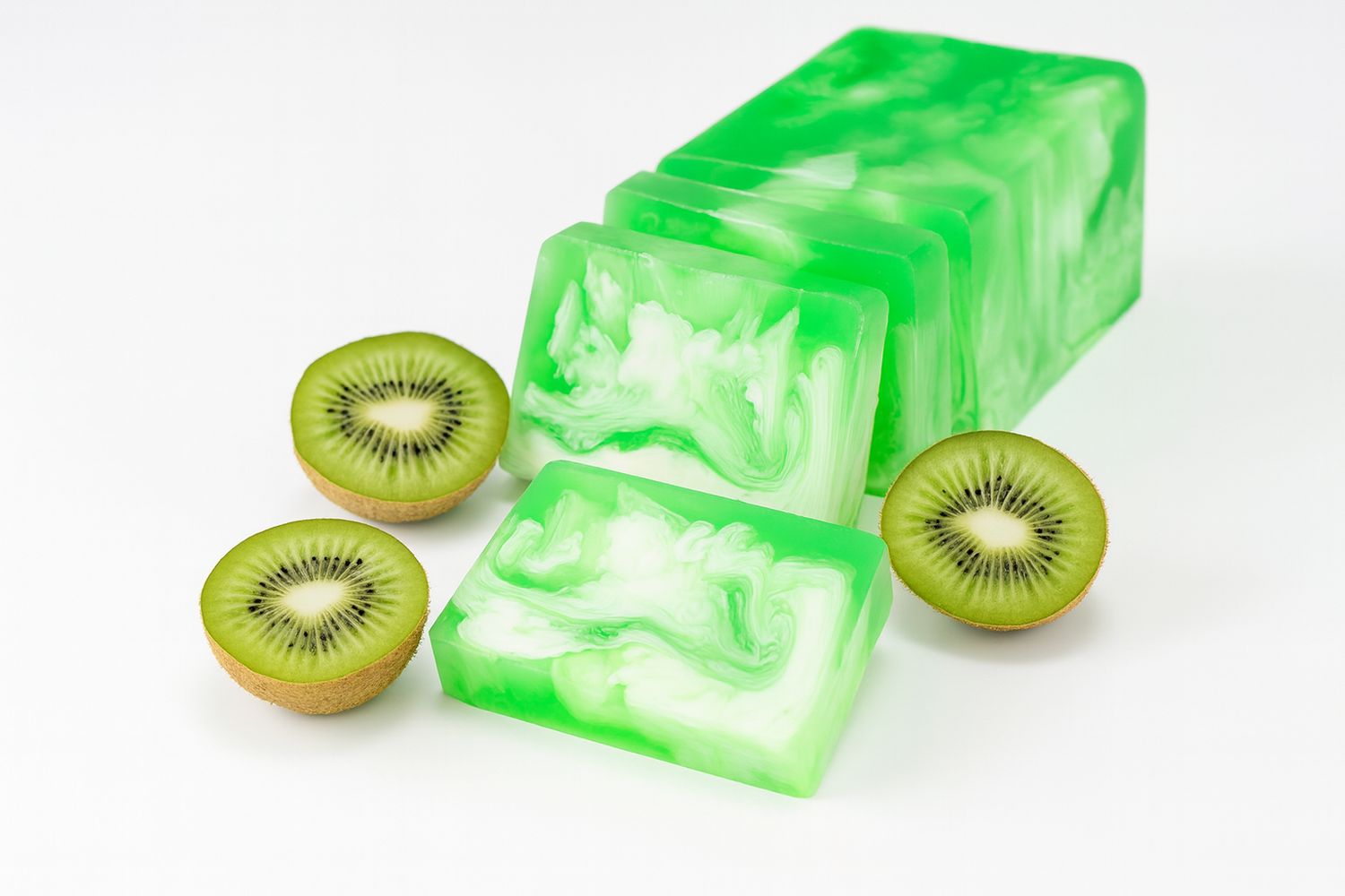 Grüne Seifenstücke mit weißer Maserung, neben halbierten Kiwis. Auf weißem Hintergrund.