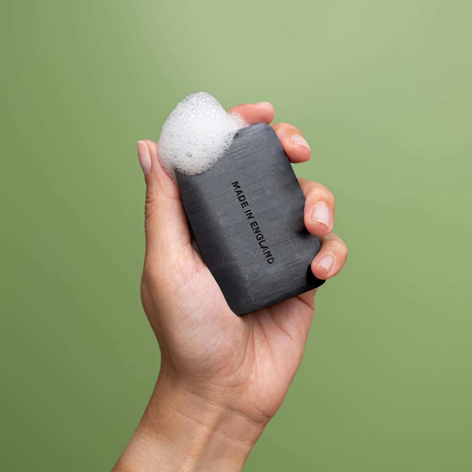 Hand hält schwarze Seife mit Schaum. Aufschrift: "Made in England".