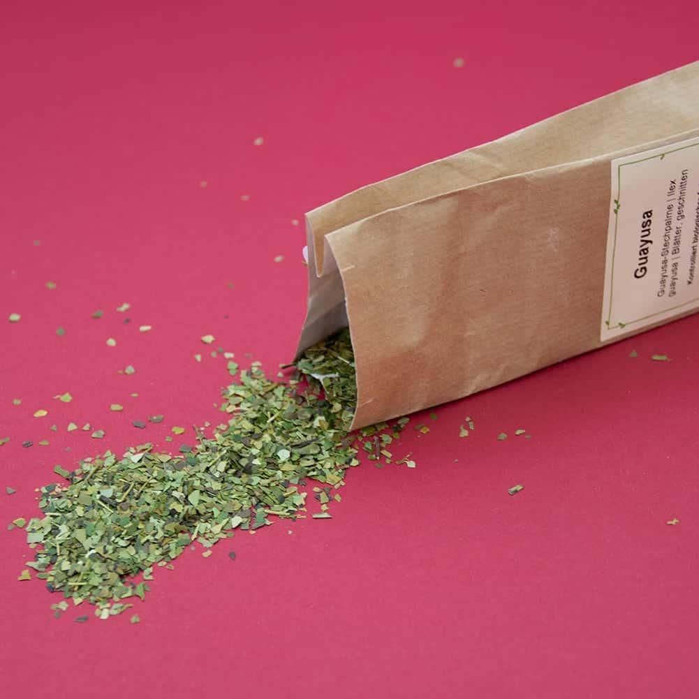 Braune Papiertüte, Guayusa-Stechpalme-Blätter fallen heraus. Etikett mit Produktname und Informationen.