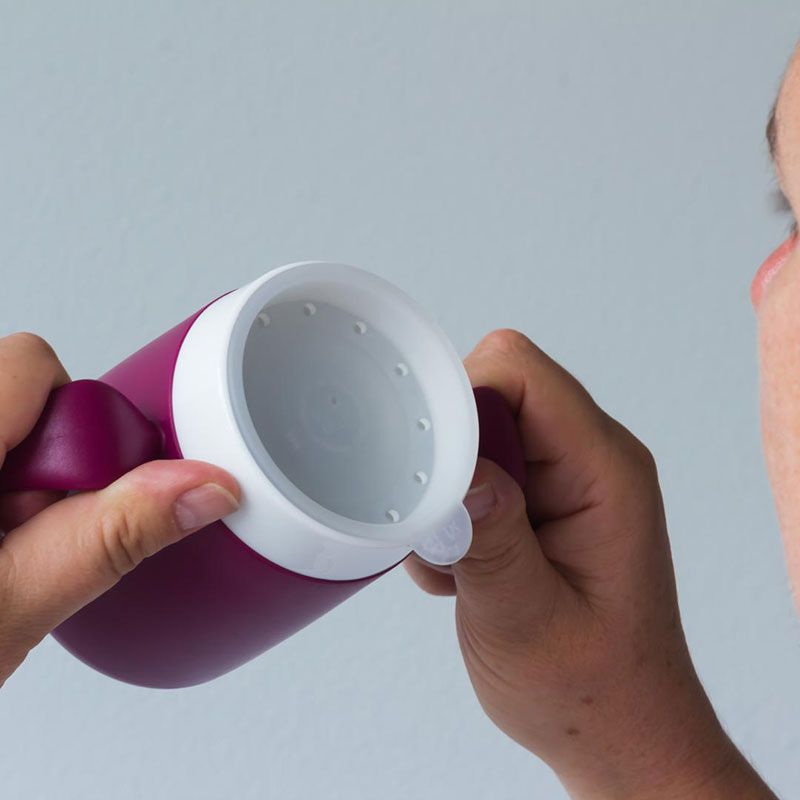 Person hält Becher mit Trinkaufsatz. Becher lila, Aufsatz weiß.