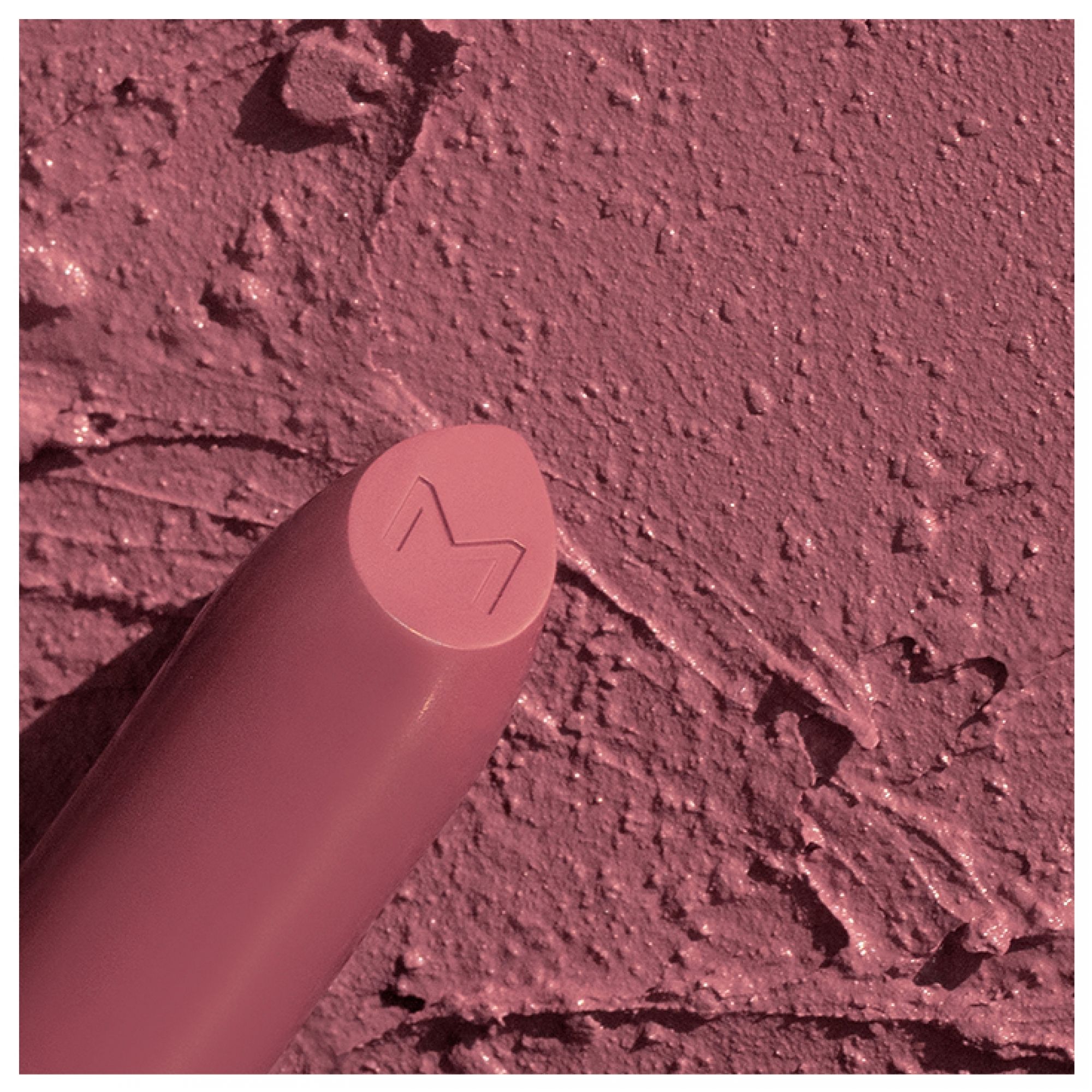 Mattes Lippenstift mit M-Logo auf der Spitze, auf einer Textur aufgetragen.