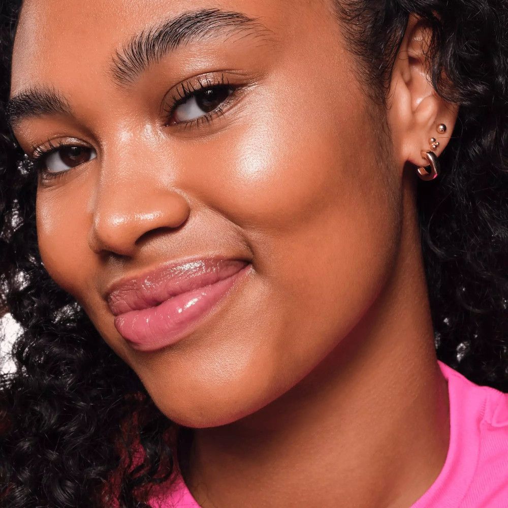 Gesicht einer Person mit Highlighter. Haut glänzt. Rosa Lippen. Ohrringe.