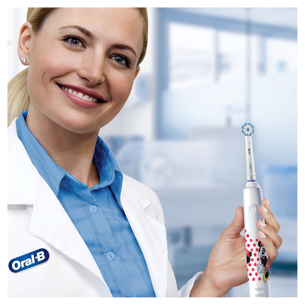 Frau hält weiße elektrische Zahnbürste "Minnie Mouse". Oral-B Logo sichtbar. Hintergrund: Büro.