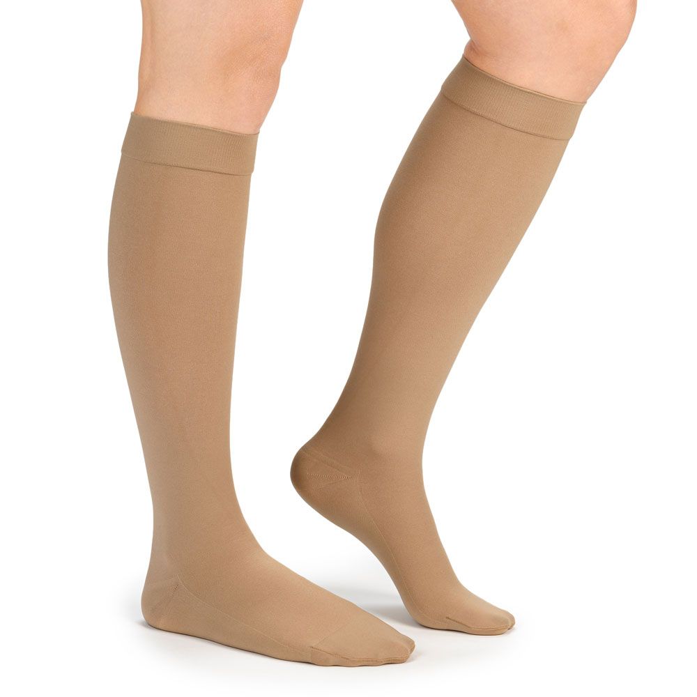 Beige Kompressionsstrümpfe am Bein. Kniestrümpfe, glatt, ohne Muster. Oberer Rand umgeschlagen.