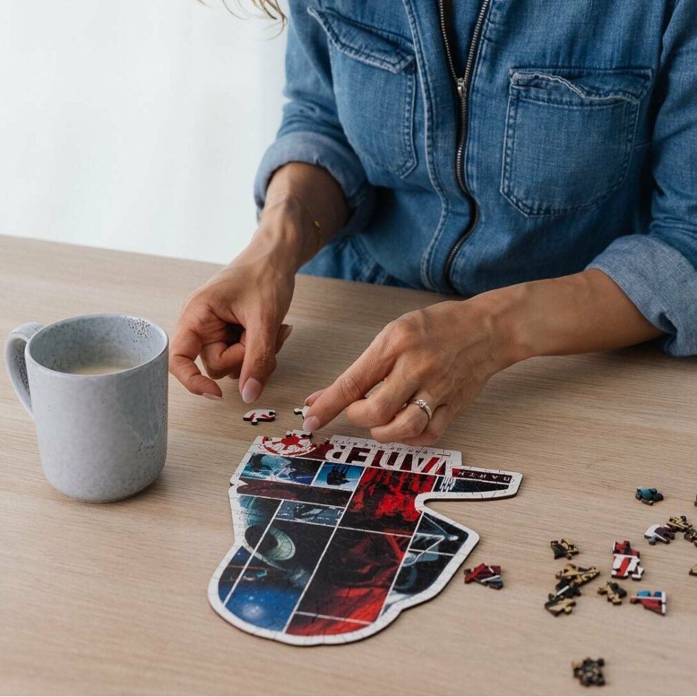 Person setzt ein Darth Vader Puzzle zusammen. Holzpuzzle mit Star Wars Motiven. Teile auf einem Tisch. Kaffeetasse daneben.