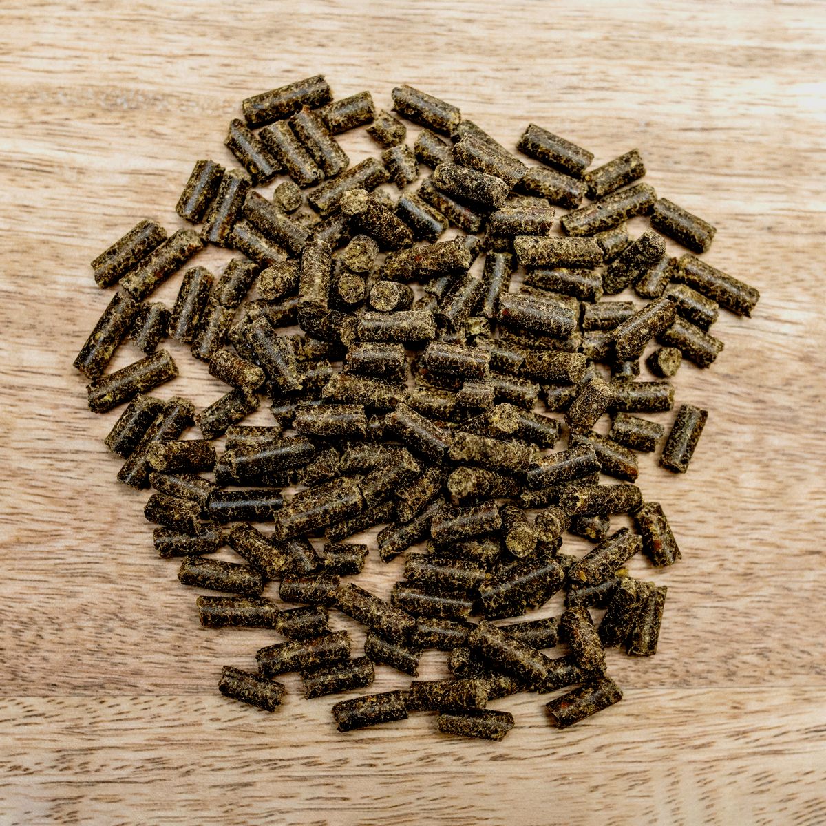 Haufen von zylindrischen Pellets auf Holzuntergrund. Dunkelgrüne Farbe, raue Textur.