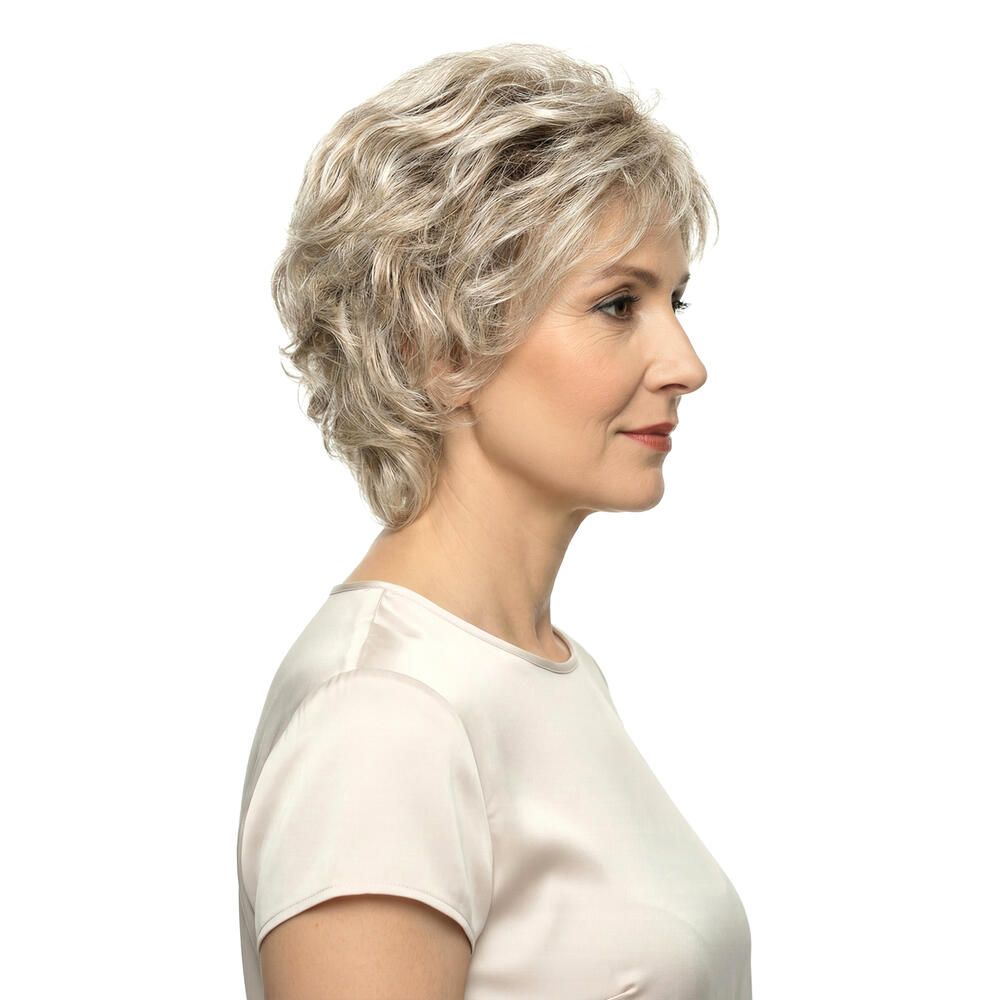 Frau mit kurzer, blond-grauer Perücke, Seitenansicht. Helles Oberteil. Weißer Hintergrund.