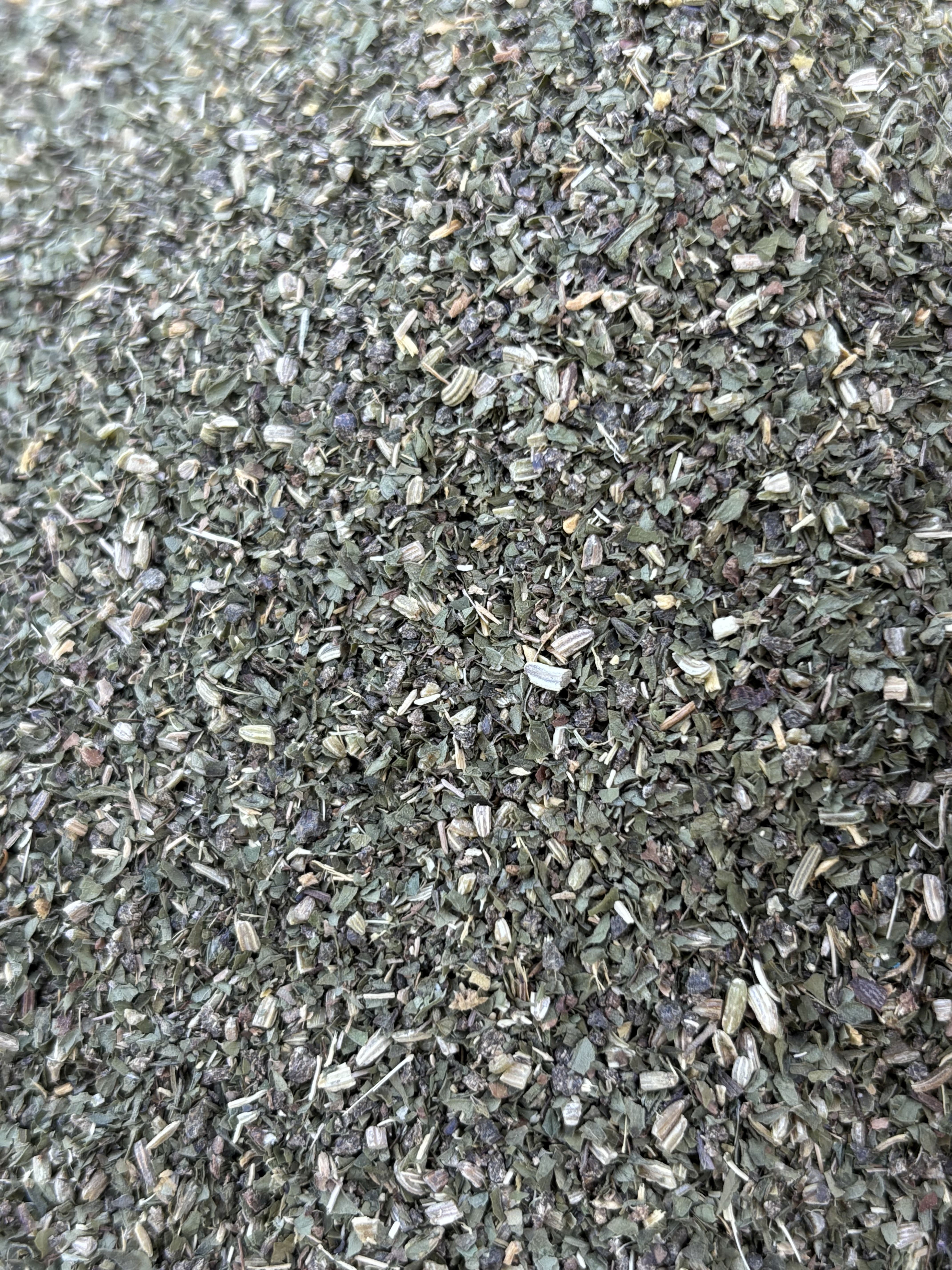 Nahaufnahme von zerkleinerten Kräutern. Grüne und braune Farbnuancen. Textur von getrockneten Blättern und Stängeln.