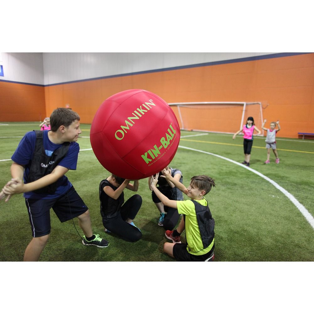 Roter Kin-Ball. Mehrere Kinder spielen in einer Sporthalle. Das Produkt wird von mehreren Kindern gehalten.