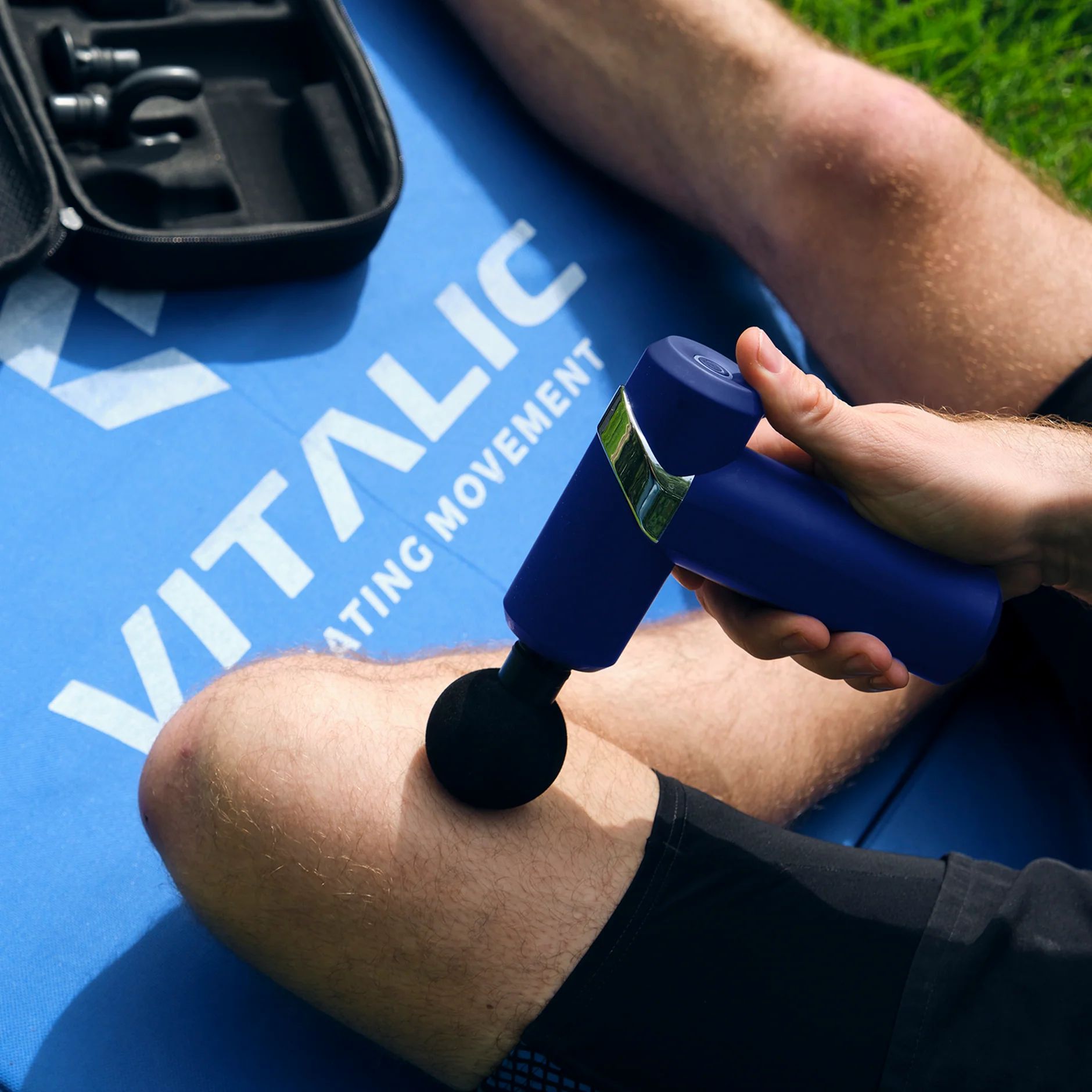 Person verwendet blaues Massagegerät am Bein. VITALIC-Logo auf Matte sichtbar.