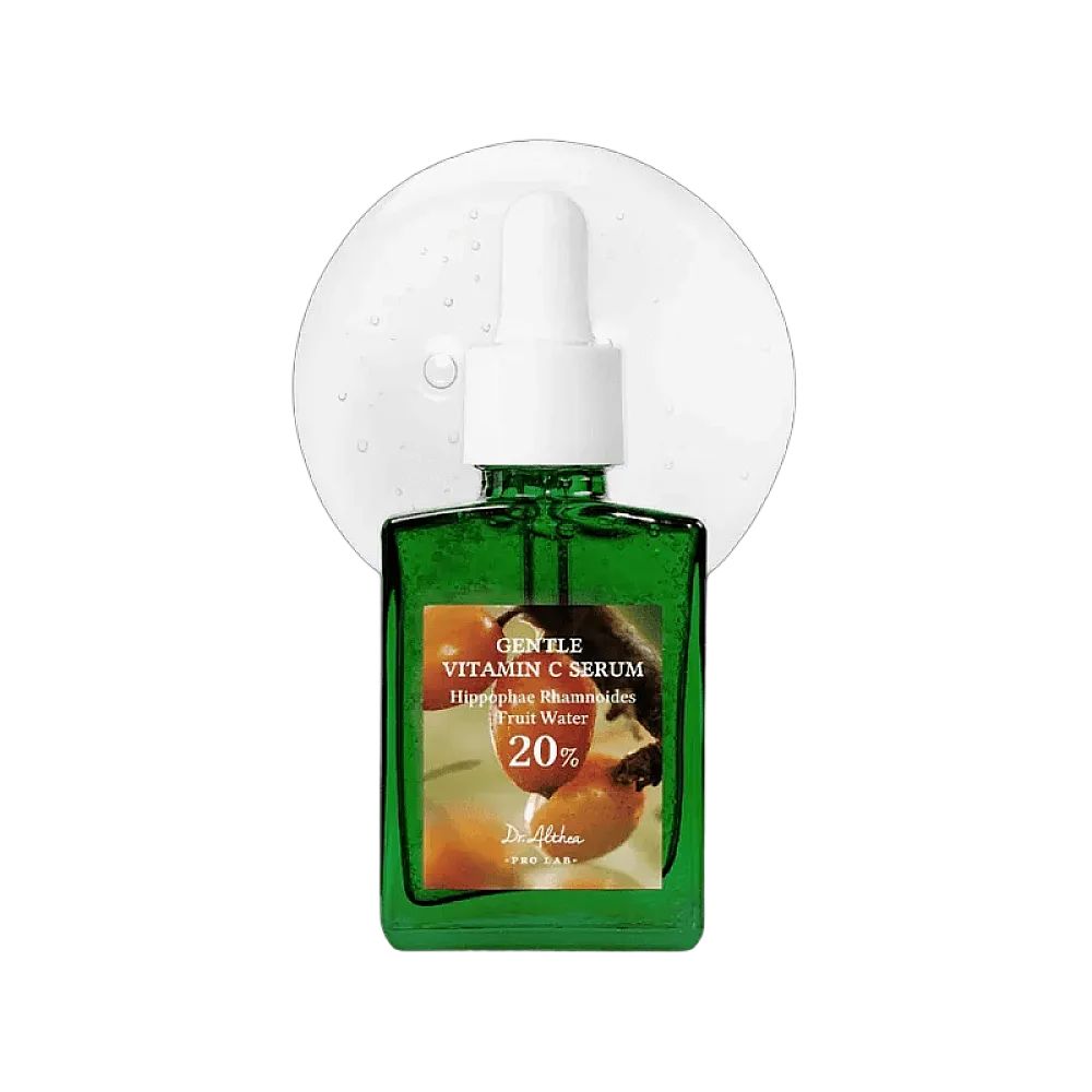 Grüne Flasche mit Serum und Pipette. Aufschrift: Gentle Vitamin C Serum, 20%. Serum-Tropfen im Hintergrund.