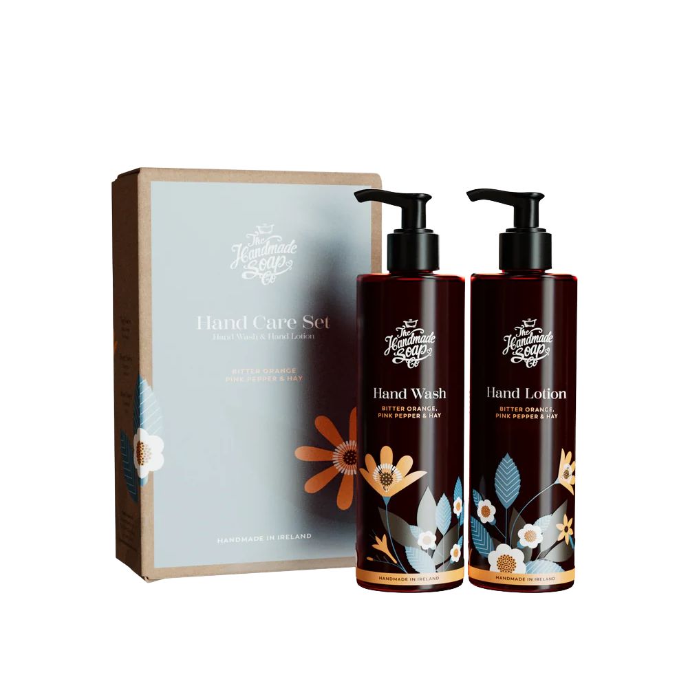 Geschenkset Handpflege. Enthält Handseife und Handlotion. Braune Flaschen mit schwarzen Pumpen. Verpackung mit floralem Design und Text.