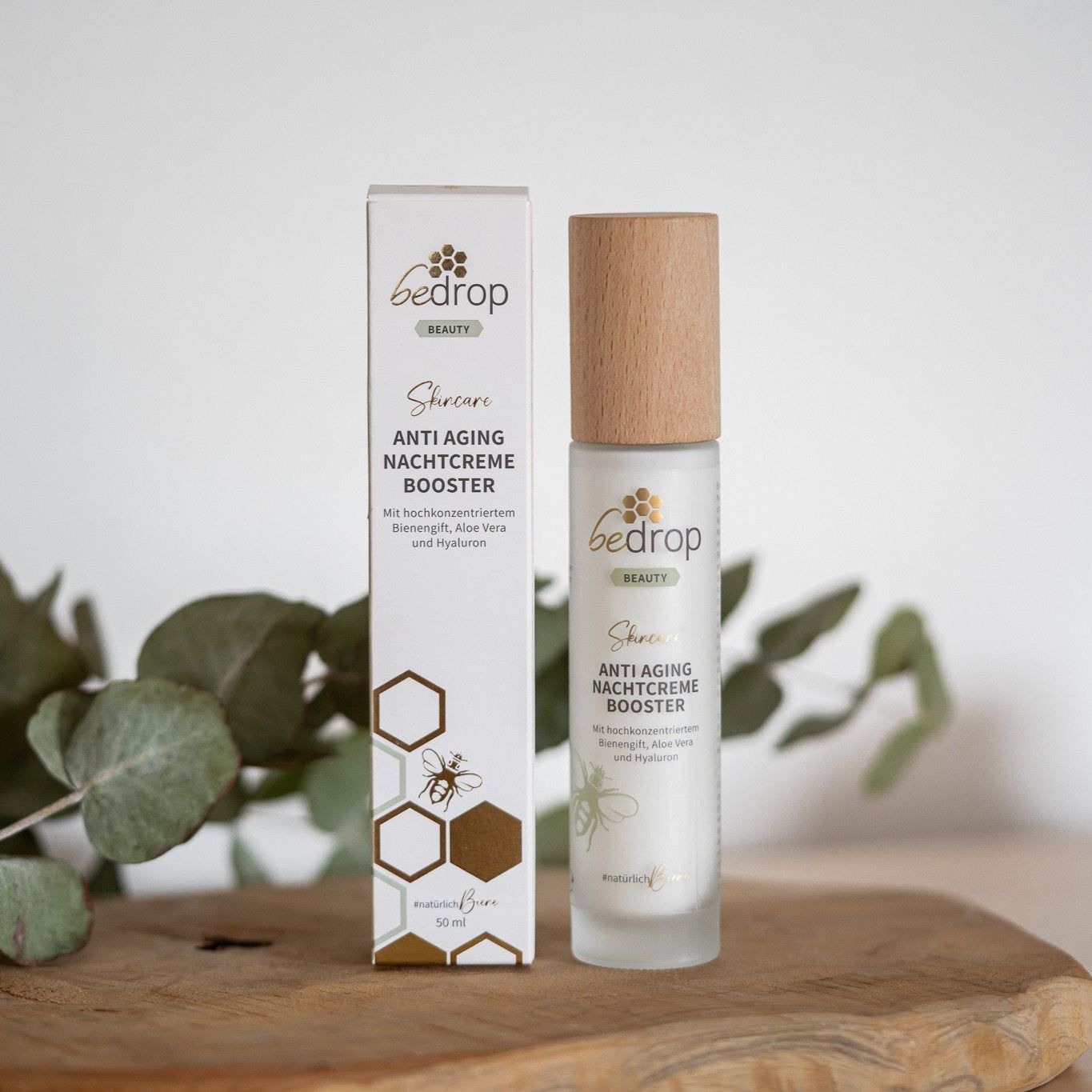 Eine Flasche und Verpackung der Anti Aging Nachtcreme Booster. Aufschrift: bedrop, Anti Aging Nachtcreme Booster, #natürlichBure. Hintergrund: Holzbrett.