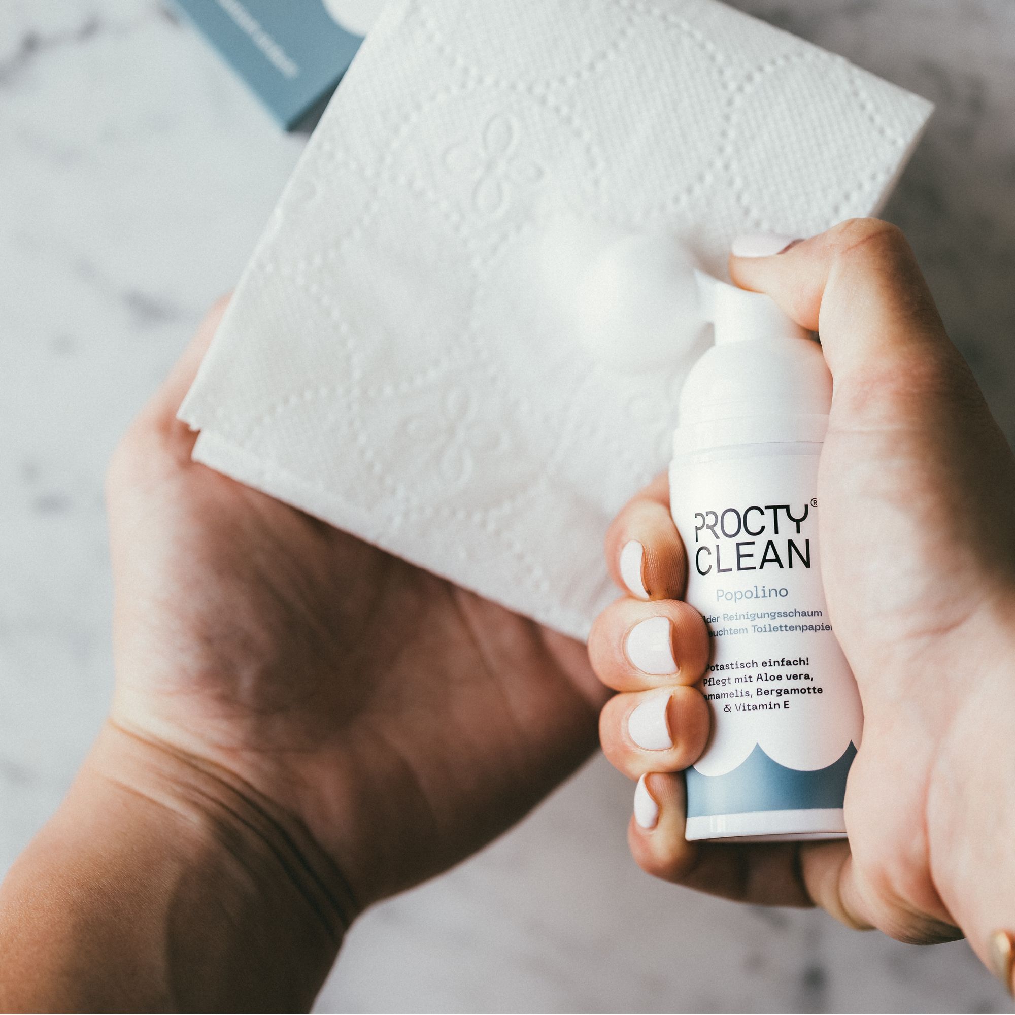 Hand hält Flasche und Toilettenpapier. Flasche: ProctyClean Popolino. Schaum auf Papier.